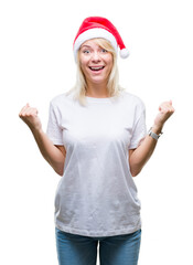 Wall Mural - Young beautiful blonde woman wearing christmas hat over isolated background celebrating surprised and amazed for success with arms raised and open eyes. Winner concept.