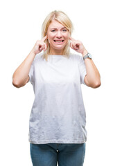 Poster - Young beautiful blonde woman wearing white t-shirt over isolated background covering ears with fingers with annoyed expression for the noise of loud music. Deaf concept.