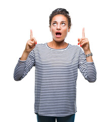 Poster - Young braided hair african american girl wearing sweater over isolated background amazed and surprised looking up and pointing with fingers and raised arms.