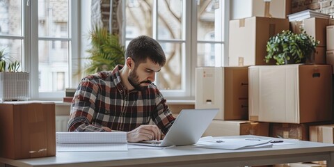 Wall Mural - the logistician is sitting at a white table and filling out invoices in a bright room next to boxes 