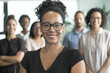 © Victor Bertrand - Smiling woman in glasses stands confidently in the front, with a supportive team blurred in the background, representing strong leadership and unity.