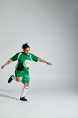 Wall Mural - A female soccer player in a green uniform juggles the ball with one foot against a white backdrop.
