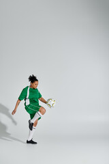 Wall Mural - A woman in a green soccer uniform juggles a white ball in a studio setting.