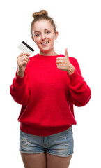 Poster - Young blonde woman holding credit card happy with big smile doing ok sign, thumb up with fingers, excellent sign