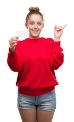 Wall Mural - Young blonde woman holding advertising card very happy pointing with hand and finger to the side