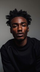 A close-up portrait of a young Black man with dreadlocks, wearing a black sweater