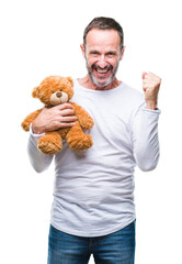 Canvas Print - Middle age senior hoary man holding teddy bear over isolated background screaming proud and celebrating victory and success very excited, cheering emotion