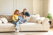 © Home-stock - Positive family of three, mother, father and daughter sitting on couch in cozy living room, enjoy time together at home, free space