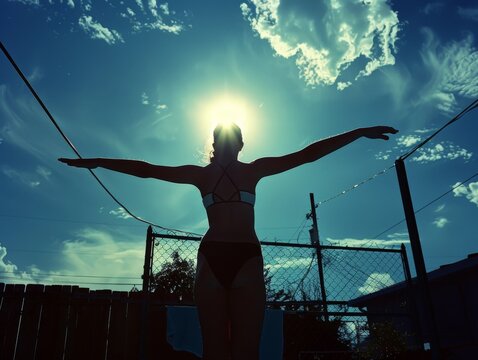 Medium shot of A beautiful woman in black leotards dancing with her arms outstretched, silhouetted against the sky, shot from behind in a movie still, minimalist style