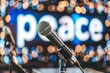 © Dina - Microphones on stage with 'peace' background, symbolizing a peace conference or public speaking for peace.