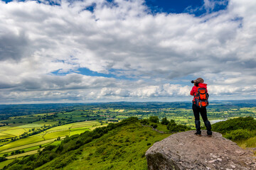 Wall Mural - Hiker taking a photograph from a hill overlooking rolling farmland (Brecon Beacons, Wales)