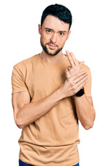 Poster - Hispanic man with beard wearing casual t shirt holding symbolic gun with hand gesture, playing killing shooting weapons, angry face