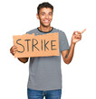 © Krakenimages.com - Young handsome african american man holding strike banner cardboard smiling happy pointing with hand and finger to the side