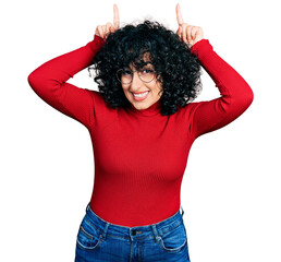 Canvas Print - Young middle east girl wearing casual clothes and glasses doing funny gesture with finger over head as bull horns