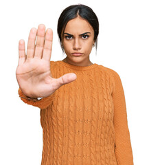 Wall Mural - Young brunette woman wearing casual winter sweater doing stop sing with palm of the hand. warning expression with negative and serious gesture on the face.