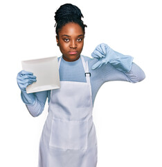 Sticker - Young african american woman wearing apron washing dishes with angry face, negative sign showing dislike with thumbs down, rejection concept