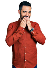 Wall Mural - Young hispanic man with beard wearing casual shirt laughing and embarrassed giggle covering mouth with hands, gossip and scandal concept