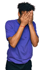 Wall Mural - Young african american man with beard wearing casual purple t shirt with sad expression covering face with hands while crying. depression concept.