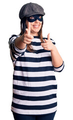 Canvas Print - Young beautiful brunette woman wearing burglar mask pointing fingers to camera with happy and funny face. good energy and vibes.