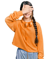 Poster - Young brunette girl with long hair wearing sweatshirt and headphones smiling and laughing with hand on face covering eyes for surprise. blind concept.