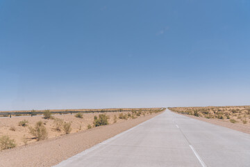 Wall Mural - A long, empty road with a clear blue sky above. The road is surrounded by a desert landscape