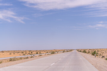 Wall Mural - A long, empty road with a clear blue sky above. The road is surrounded by a desert landscape