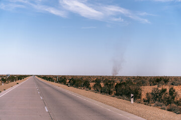 Wall Mural - A road with a few trees in the background. The sky is clear and blue. There is a car on the road