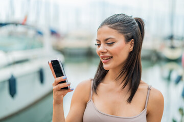 Wall Mural - Young pretty woman using mobile phone at outdoors with happy expression