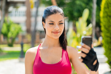 Wall Mural - Young pretty sport woman at outdoors sending a message or email with the mobile