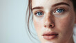 © VK Studio - A close-up portrait of a young woman with blue eyes and freckles bathed in soft light, capturing an intimate moment of natural beauty.
