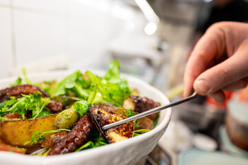 Wall Mural - Close-up of hand serving a salad with mixed greens, avocado, and grilled vegetables using tongs