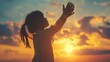 © atipong - Silhouette of kid child girl raised hands worship pray. Kid girl praying in the sunset sky for a new day freedom