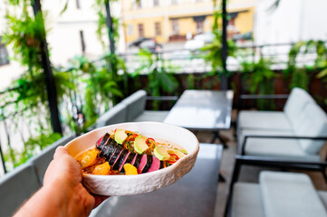 Wall Mural - A hand holds a colorful food bowl against a blurred outdoor seating area.