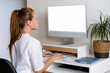 © Barillo_Images - A female medical worker works at a computer. Mockup blank screen of computer monitor in hospital office. Online consultation with doctor. Telemedicine.