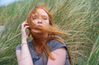 © ullision - young red-haired woman with the wind blowing her hair into her face sits on vacation in the windy sand dunes of St. Peter Ording