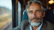© svastix - A mature man with silver hair and a grey beard, dressed in a dark coat, gazes thoughtfully out of a train window, suggesting a reflective mood during his journey.