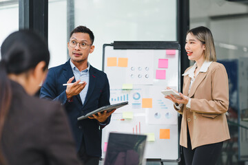 Wall Mural - Confident businessman leading a meeting, engaging with colleagues while presenting data charts and graphs in a modern office.