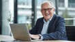 © The Little Hut - Business portrait  businessman sitting in in office working with laptop computer Mature age middle age mid adult man in 50s with happy confident smile Copy space : Generative AI