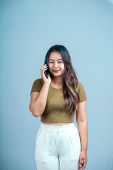 Wall Mural - A young Asian woman with an expression holding a smartphone isolated on a blue background