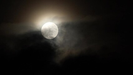 Wall Mural - The full moon shines through the clouds floating above the ground at night.