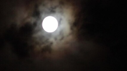Wall Mural - The full moon shines through the clouds floating above the ground at night.