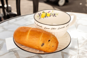One aromatic bun with a ceramic cup and saucer on a table in a cafe, close-up, isolated on a white background.