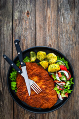 Poster - Crispy breaded fried pork chop, boiled potatoes and fresh vegetables served on black plate on wooden table
