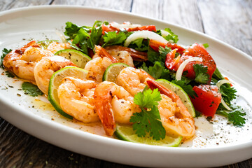 Wall Mural - Fried shrimps with garlic, lime and fresh vegetables served on white plate on wooden table
