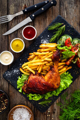 Wall Mural - Oven roasted chicken thigh with French fries and fresh vegetables on wooden table
