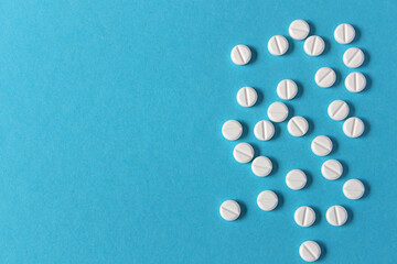 White round prescription pills with a score line are scattered on a blue background with copy space