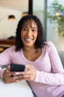 © Wavebreak Media - Woman holding smartphone and smiling, relaxing on couch at home