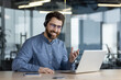 © Tetiana - A smiling young man wearing a headset is sitting in the office at the desk and talking online on a video call, gesturing with his hands