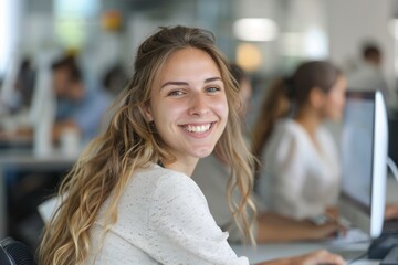 Happy young caucasian woman employee in front of computer in modern office with colleagues. Beautiful manager smiling, working on financial and marketing projects