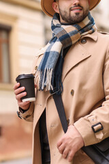 Wall Mural - Smiling man in warm scarf with paper cup outdoors, closeup